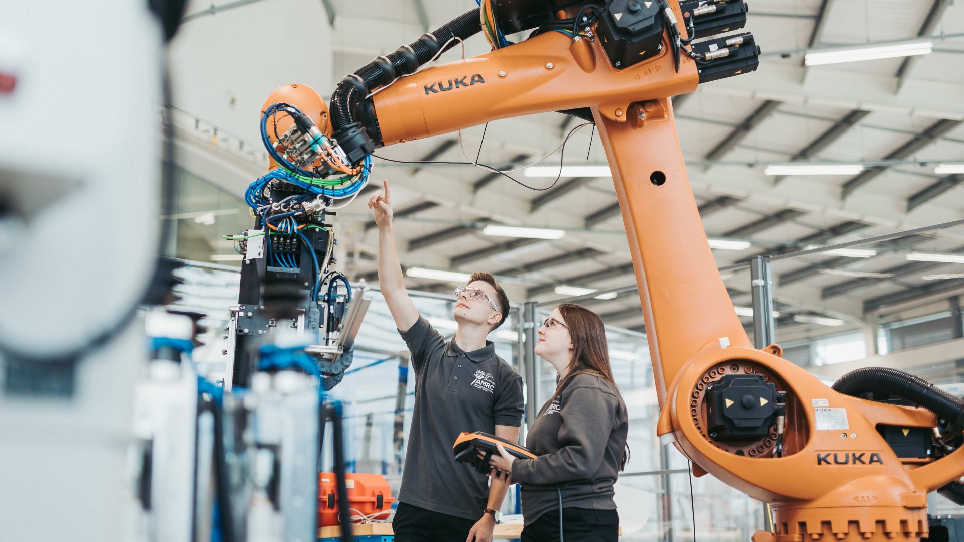 Two technicians monitor a robot working in an advanced manufacturing plant.