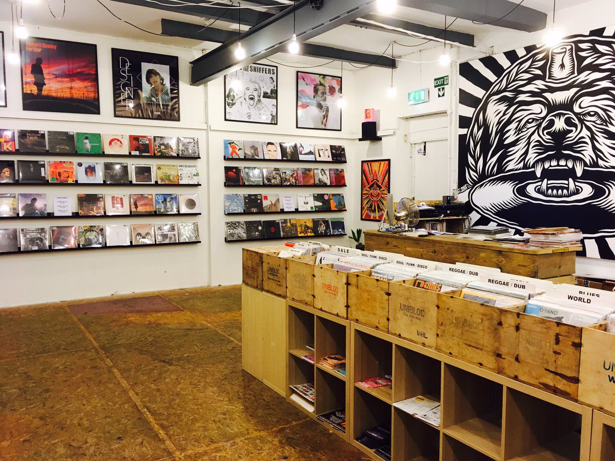 Inside Bear Tree Record, there are rows of wooden units holding records. On the walls new releases are displayed. One section of the wall has a floor to ceiling mural of the Bear Tree Records logo, painted by Sheffield artist Tom J Newell.