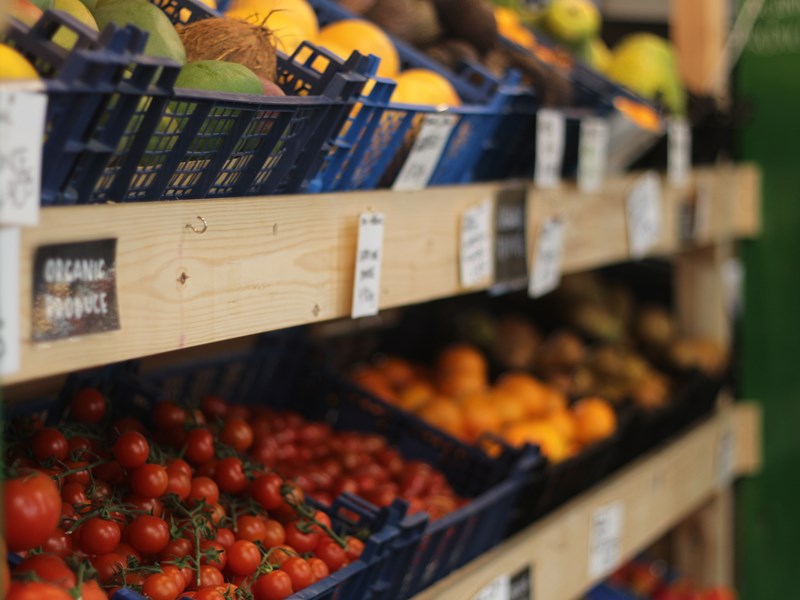 Wooden shelves with crates full of tomatoes, mangoes, coconuts and oranges.