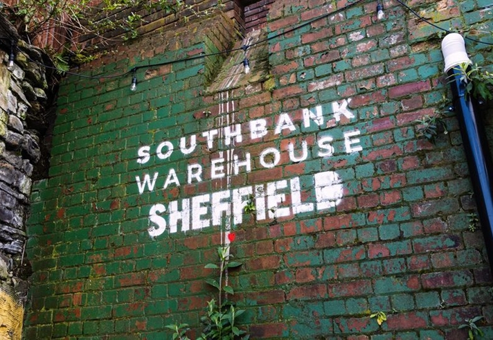 Southbank Warehouse stencilled on to a red brick wall that is partially covered in peeling green paint.