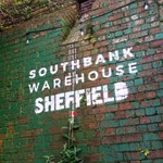 Southbank Warehouse stencilled on to a red brick wall that is partially covered in peeling green paint.