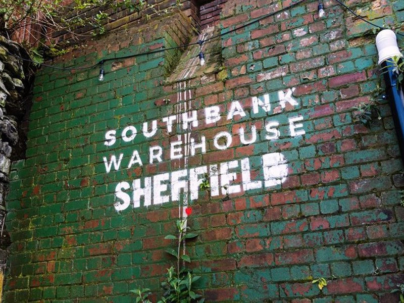 Southbank Warehouse stencilled on to a red brick wall that is partially covered in peeling green paint.