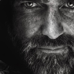 A dark, moody composition featuring a close-up of a textured black leather surface on the left side, partially illuminated by soft light. The background fades into deep shadows, creating a dramatic contrast between the highlighted material and the surrounding darkness.