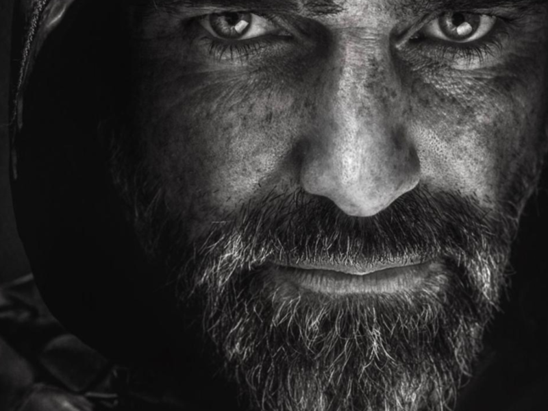 A dark, moody composition featuring a close-up of a textured black leather surface on the left side, partially illuminated by soft light. The background fades into deep shadows, creating a dramatic contrast between the highlighted material and the surrounding darkness.