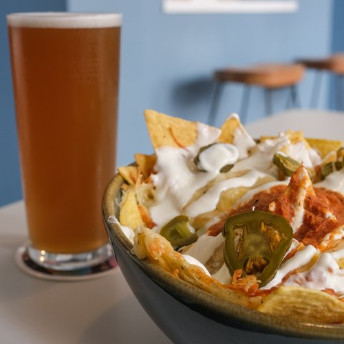A drink and a bowl of nachos covered in melted cheese, sour cream and jalapenos.