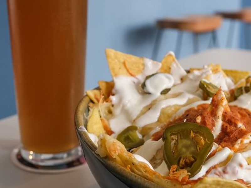 A drink and a bowl of nachos covered in melted cheese, sour cream and jalapenos.