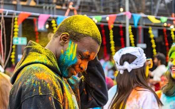 Person with bowed head covered in luminous paint at vibrant and colourful festival.