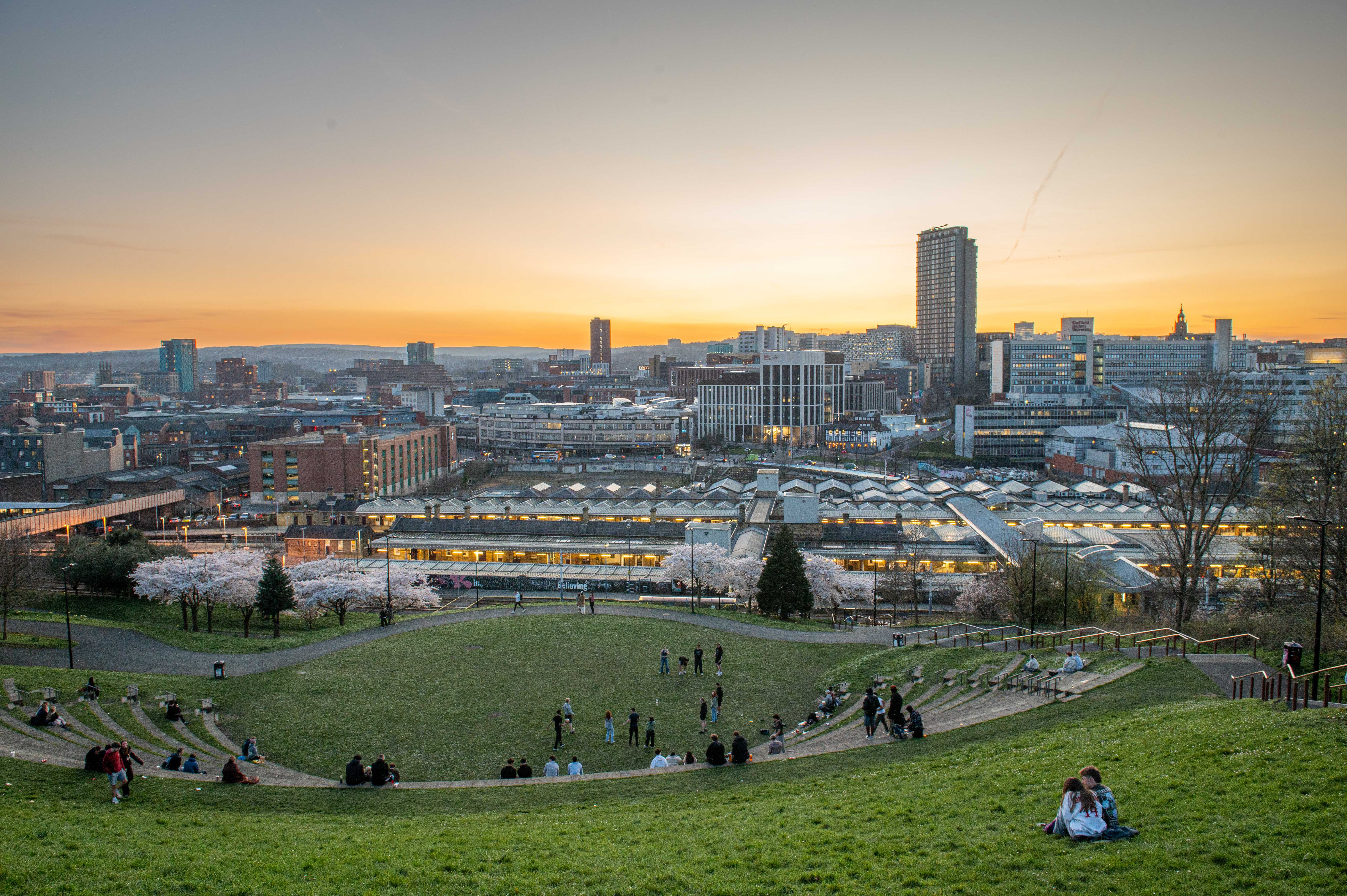 A striking cityscape view of Sheffield at dusk taken from South Street Park amphitheatre during springtime with blossom on the trees