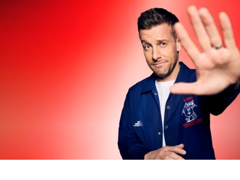 A promo shot of Chris Ramsey holding his hand up, towards the camera.