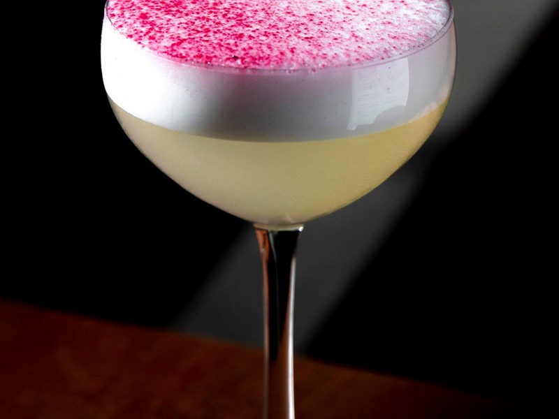 A yellow cocktails with a pink dusting on top.