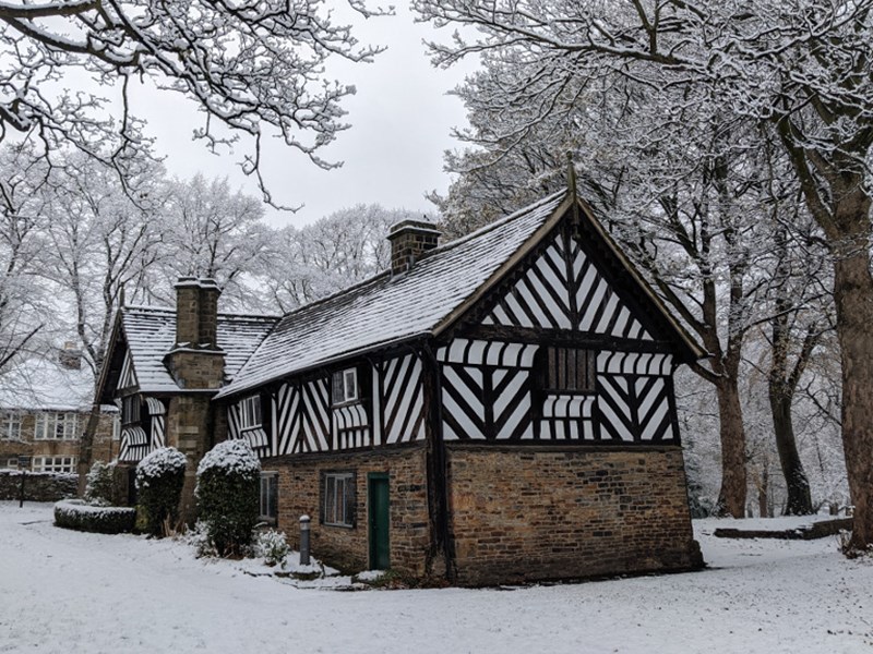 The Bishop's House in the snow. The bottom half of the building is stone and the top half is black and white timbers.