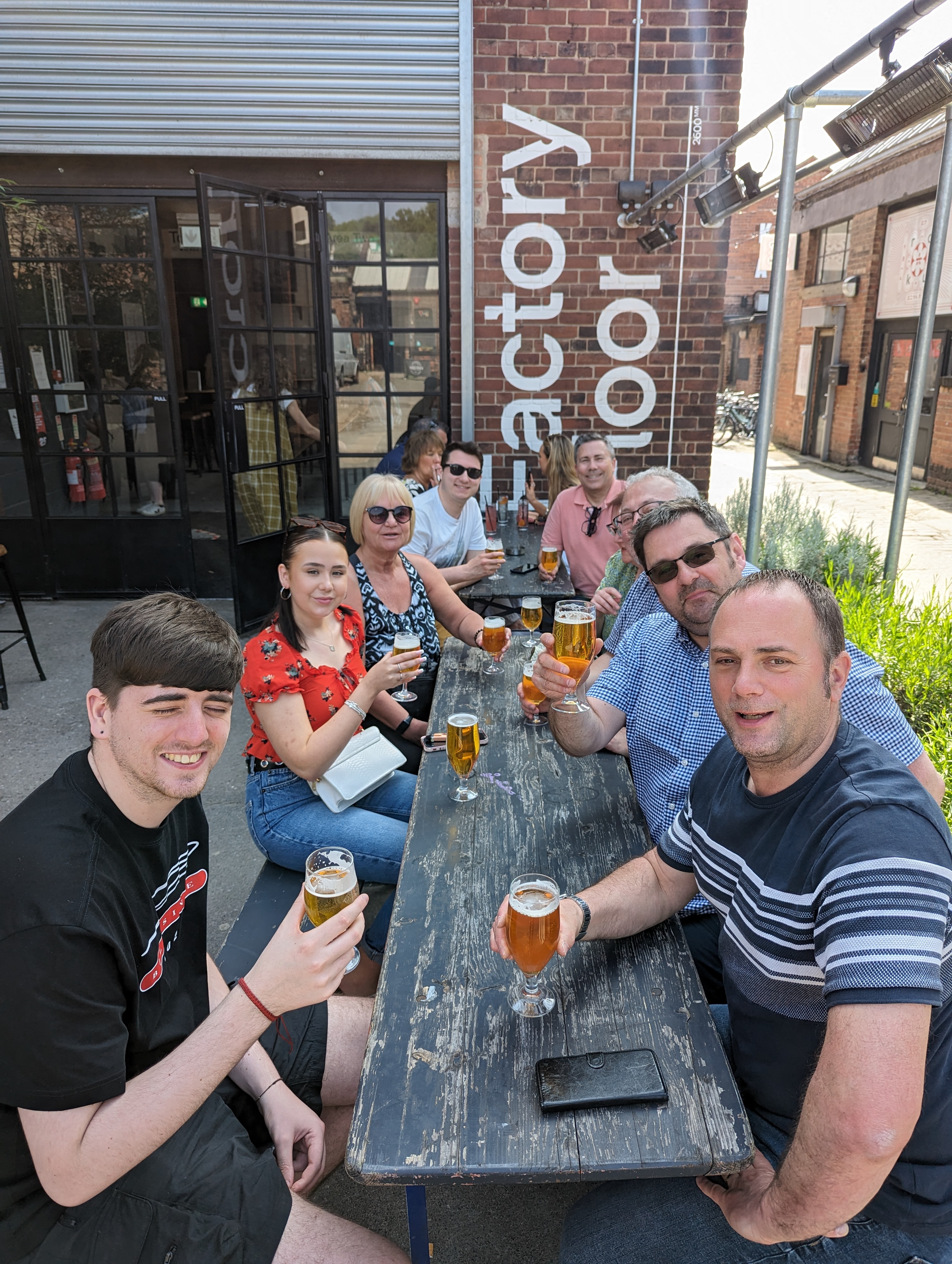 A group of people sat round a table, outside a restaurant, drinking beers.