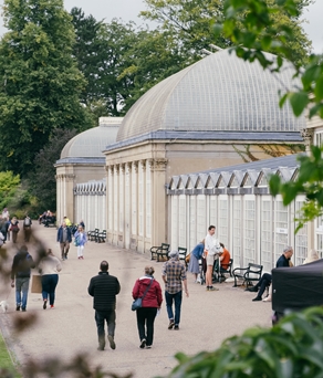 People are strolling along the wide path that runs along the length of the glass house in Sheffield Botanical Gardens.