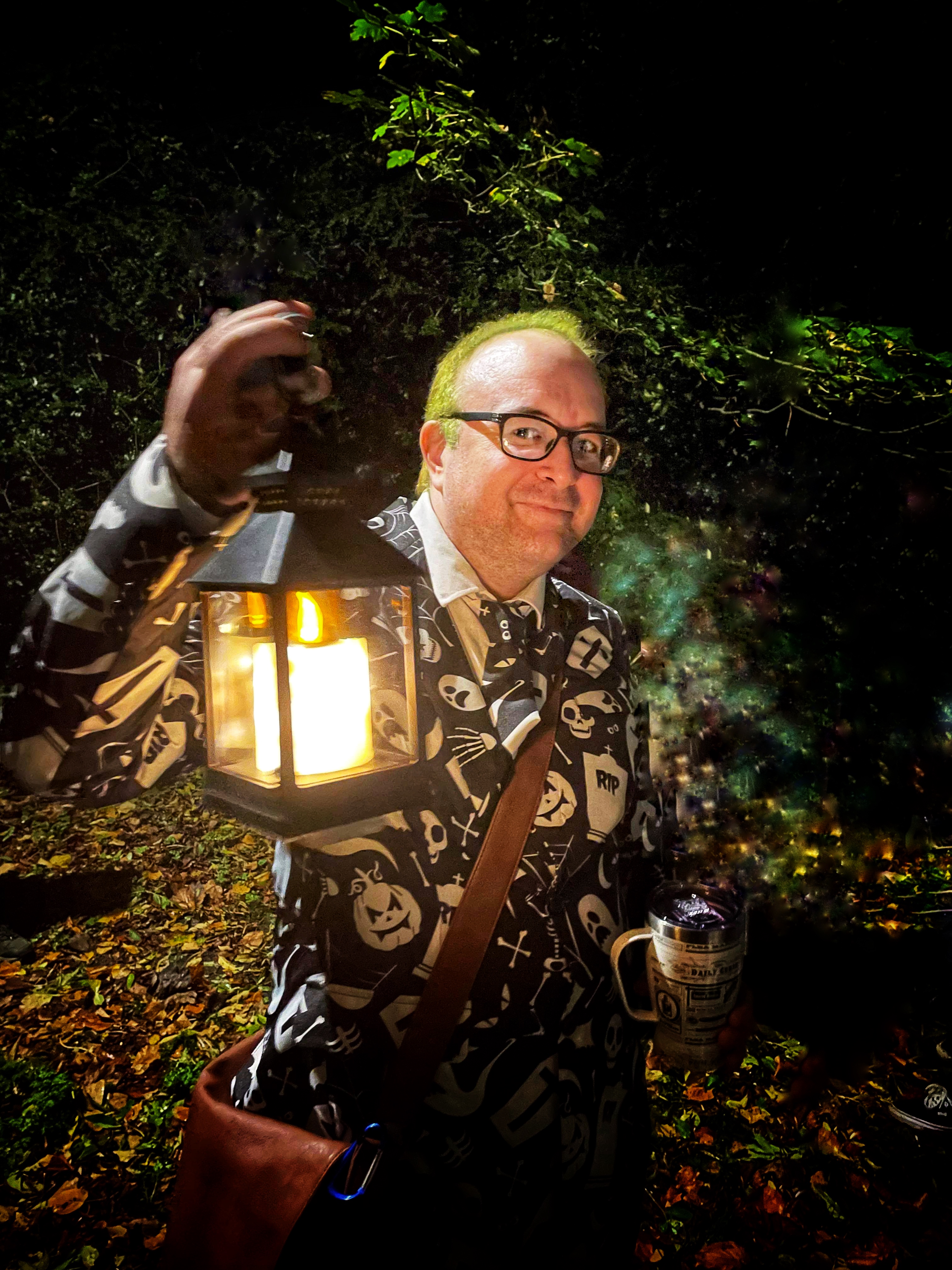 A man in a Halloween themed suit holding an old fashioned lantern.