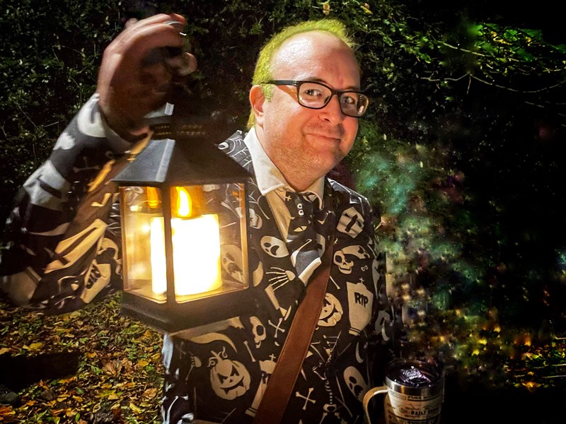 A man in a Halloween themed suit holding an old fashioned lantern.