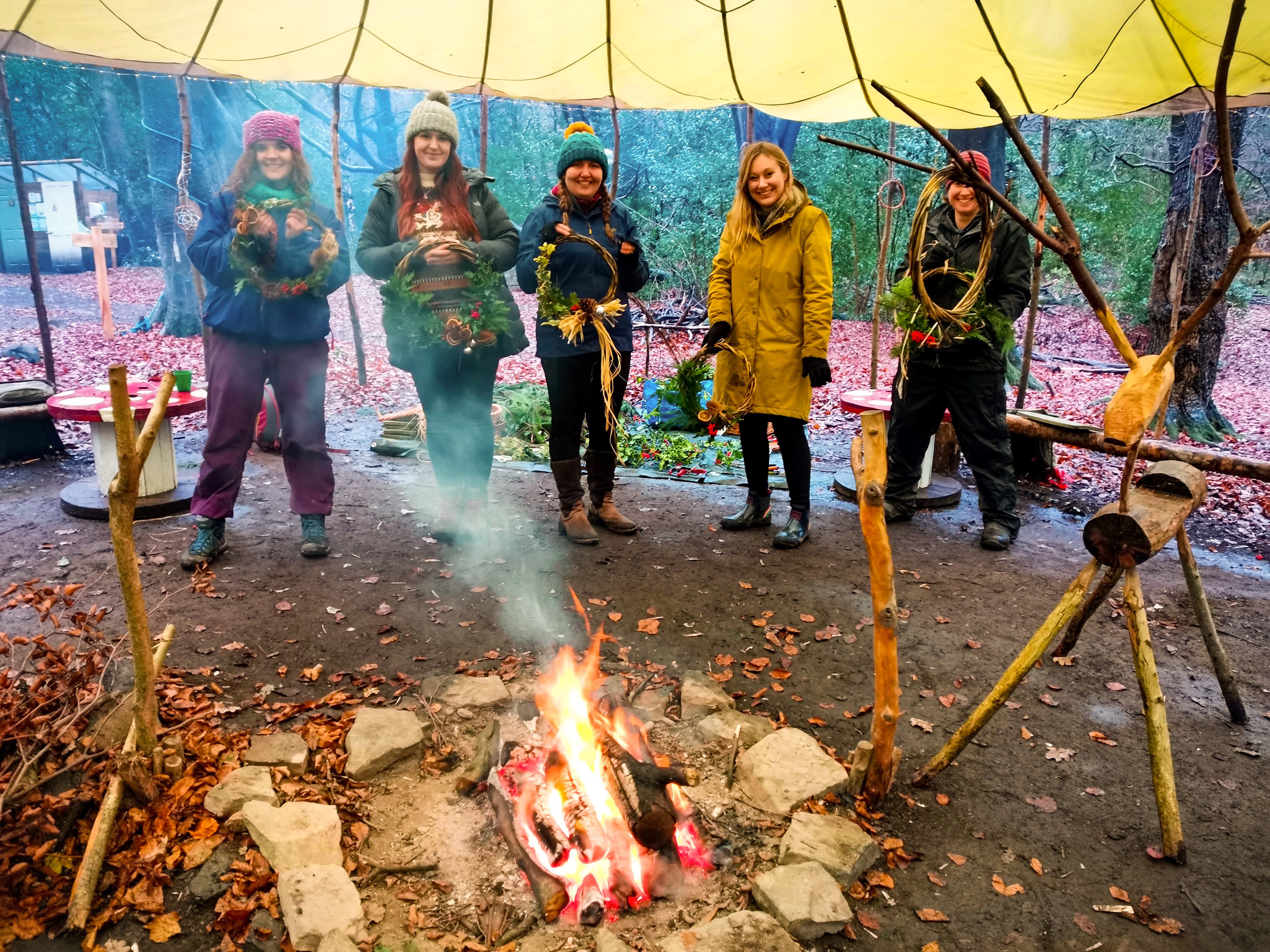 Five women are holding up wreaths they have made at TRIBE Bushcraft Centre.