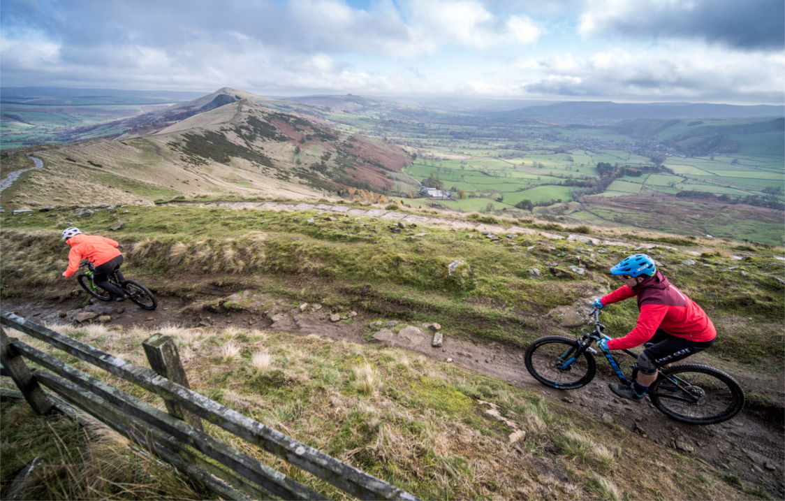 Two people mountain biking along a muddy track out in the countryside.