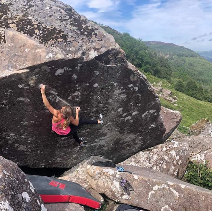 A woman climbing on a large rock. There is a thick safety mat on the ground below her.
