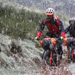 Two people cycling along a track in the countryside, in heavy rain.