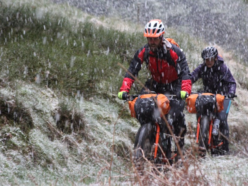 Two people cycling along a track in the countryside, in heavy rain.