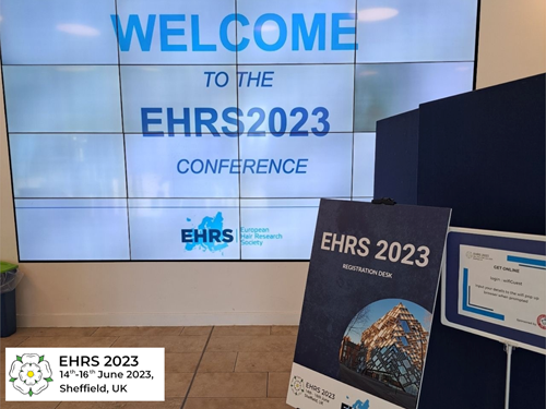 A large digital display with the text “WELCOME TO THE EHRS2023 CONFERENCE” in blue capital letters. Below the text is the European Hair Research Society logo. In the foreground, a dark signboard reads “EHRS 2023 Registration Desk” with an image of a modern glass building. Another smaller sign to the right provides instructions for online registration. A logo in the bottom-left corner indicates “EHRS 2023, 14th–16th June 2023, Sheffield, UK.”