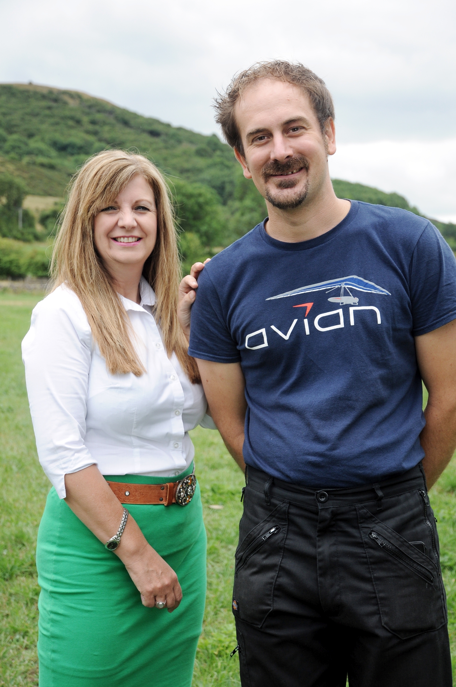 A man and a woman standing in a field. The man is wearing an Avian Hang Gliding branded t-shirt.