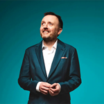 A portrait of Chris Mccausland, in a smart green suit, smiling.