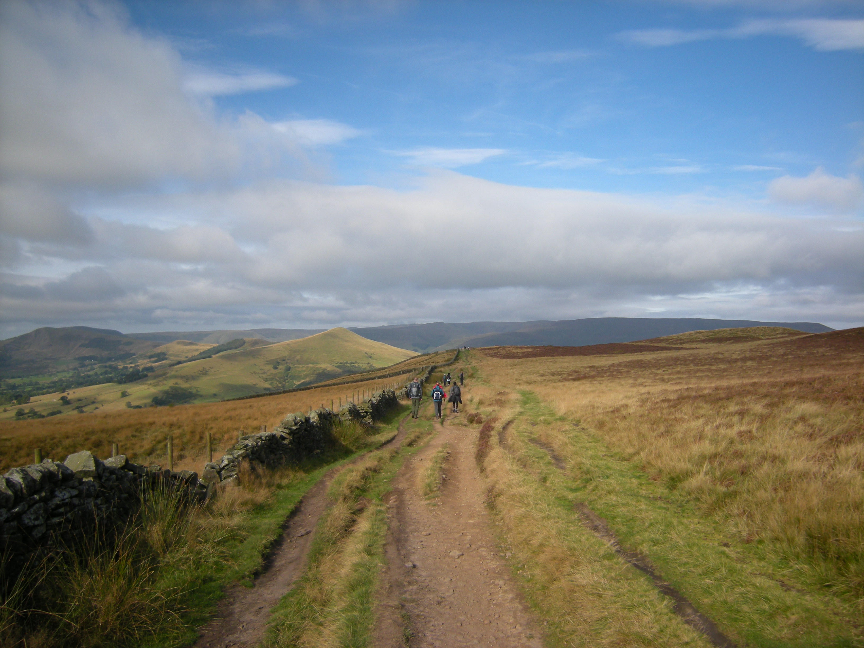 A rough track winding through hills in the countryside. In the distance you can see various groups of people out walking.