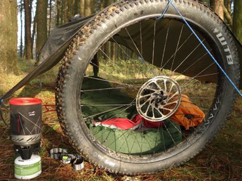 A tarpaulin and a bike wheel used to make a shelter in a wood.