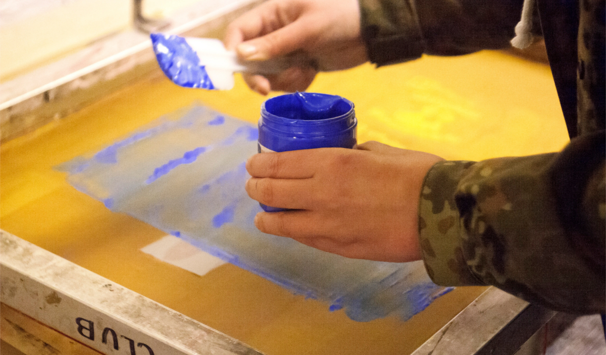 A person loading blue ink onto a printing screen.
