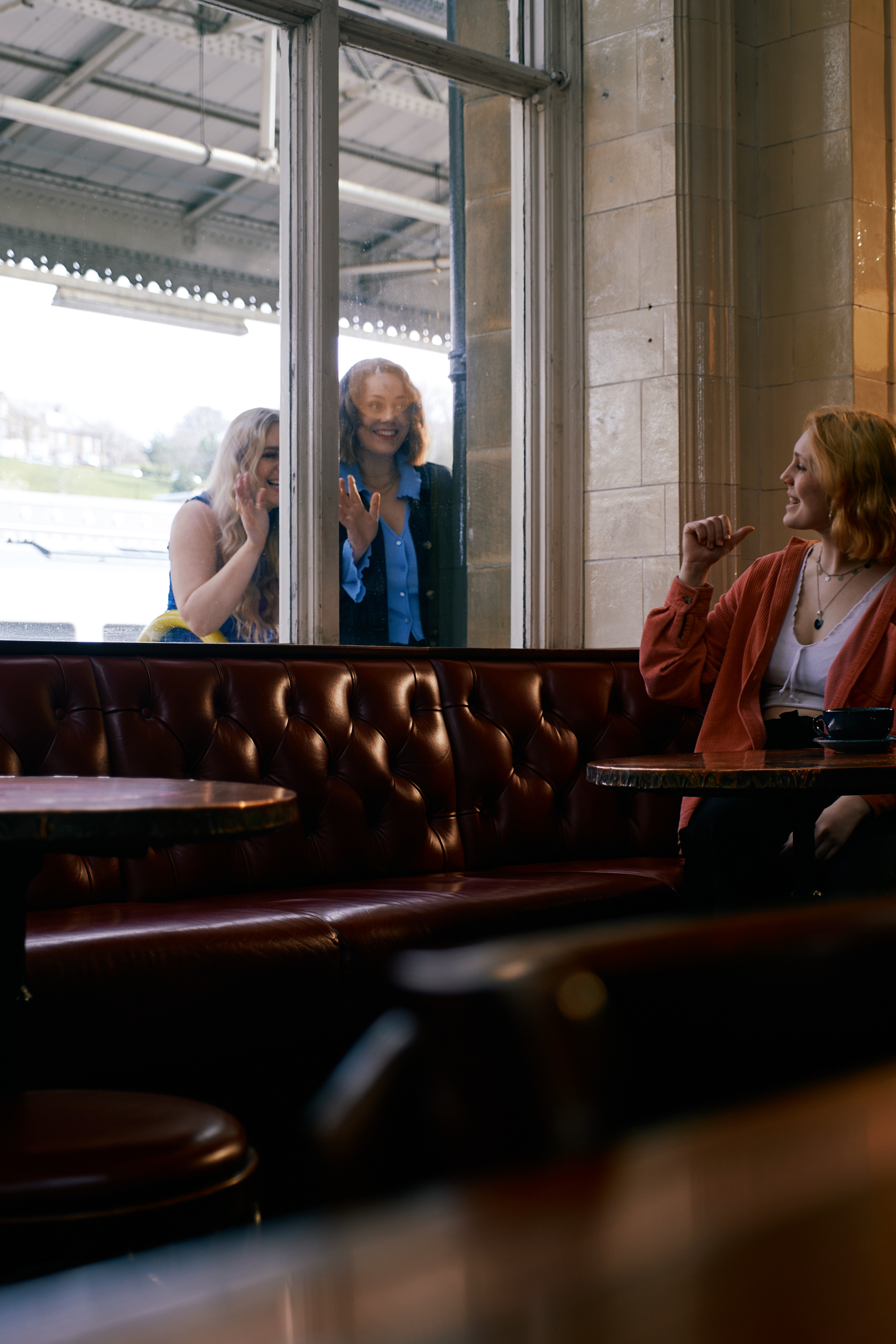 Two women stand outside a window at The Sheffield Tap, while a third (sat inside) gestures for them to come in.