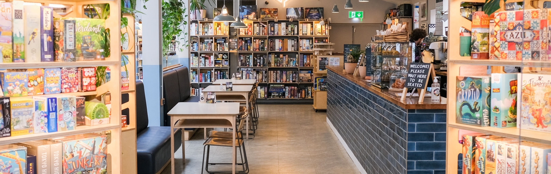 Inside The Treehouse Cafe. You can see tables and chairs, the counter and three shelving units full of board games.