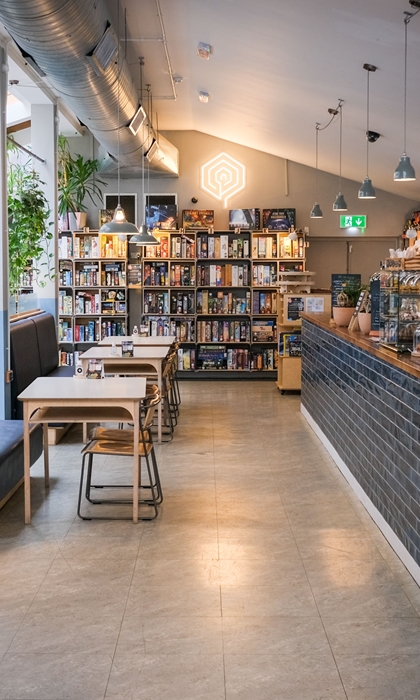 Inside The Treehouse Cafe. You can see tables and chairs, the counter and three shelving units full of board games.