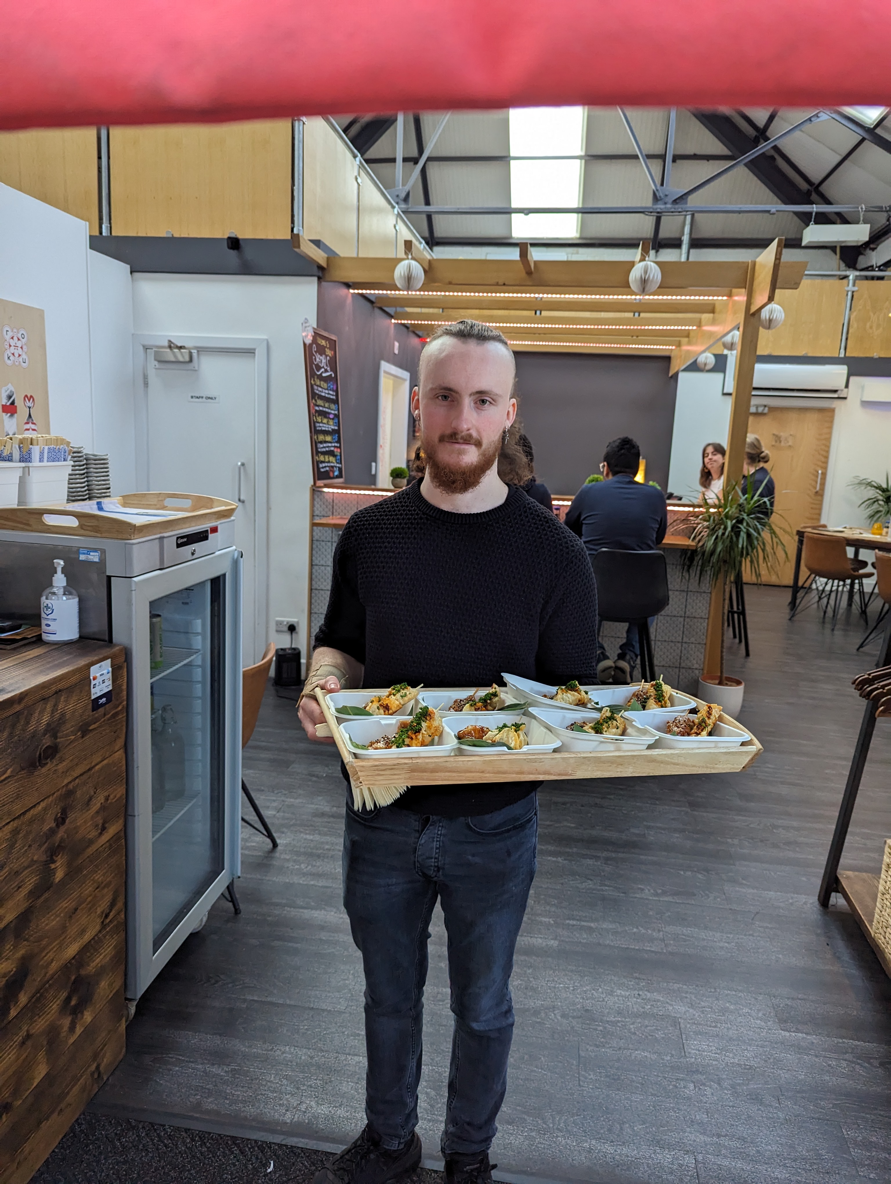 A man carrying a large tray with 8 plates of food in a restaurant.