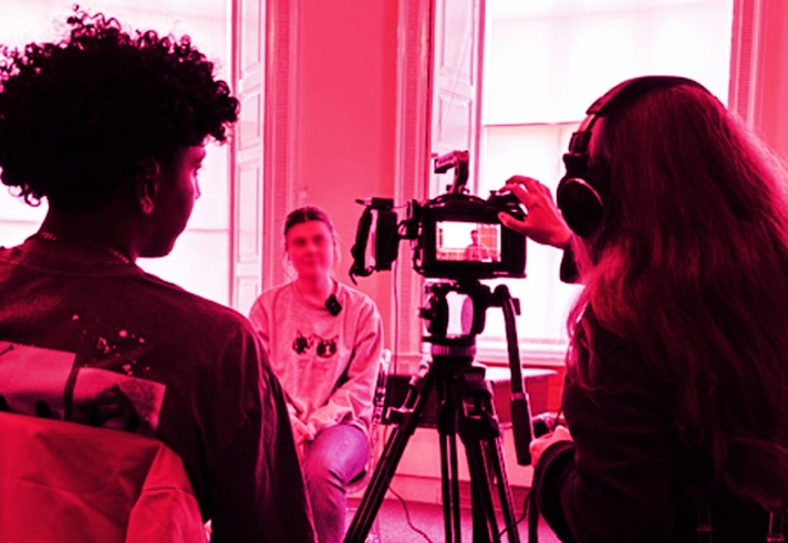 Two people filming a person on a camera.