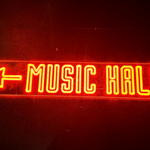 A red neon sign that reads 'Music Hall' with an arrow pointing left.