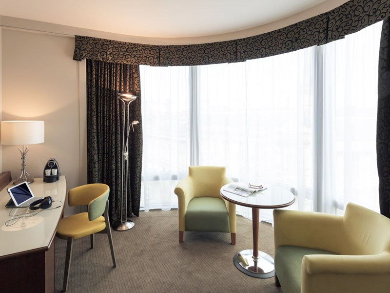 Spacious sitting area in a junior suite featuring a coffee table, armchair, and large windows with natural light
