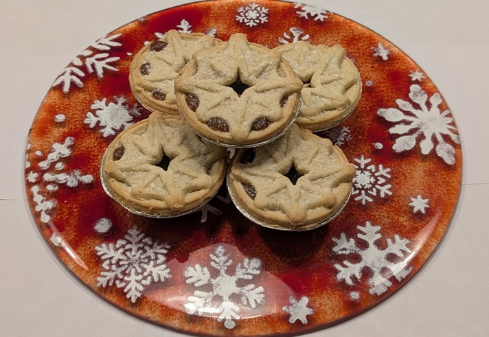 Five mince pies with star-shaped pastry tops arranged on a festive red plate decorated with white snowflakes.
