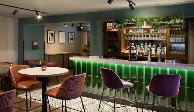 Hotel bar area with a green front, surrounded by tables and chairs for guests.