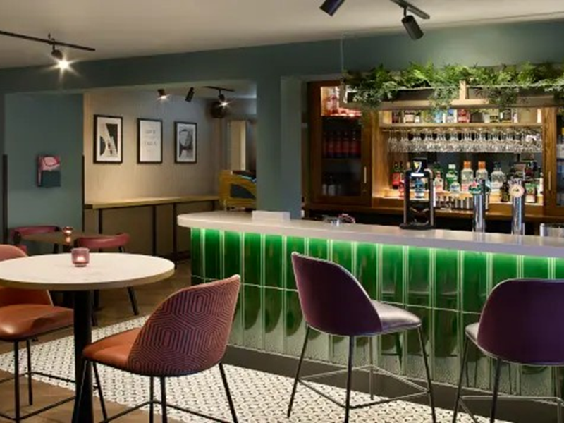 Hotel bar area with a green front, surrounded by tables and chairs for guests.