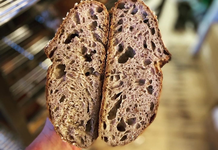 A hand holds a load of bread that has been cut in half.