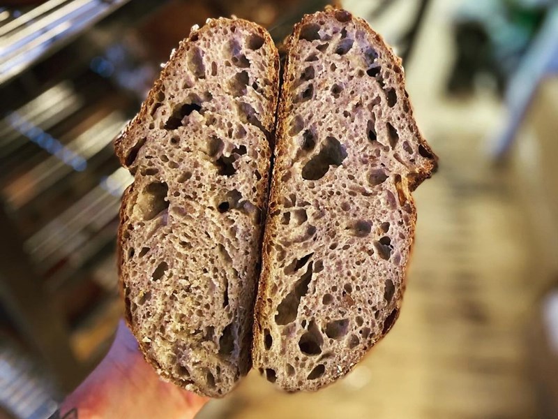 A hand holds a load of bread that has been cut in half.