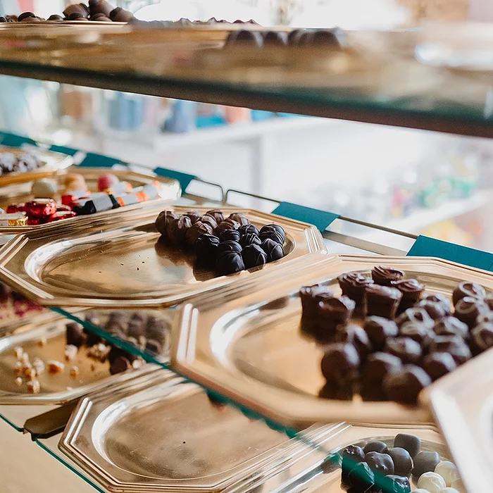 A glass cabinet, with multiple shelves, filled with all different types of chocolates.