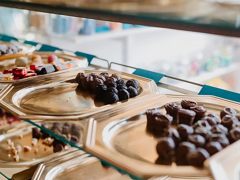 A glass cabinet, with multiple shelves, filled with all different types of chocolates.