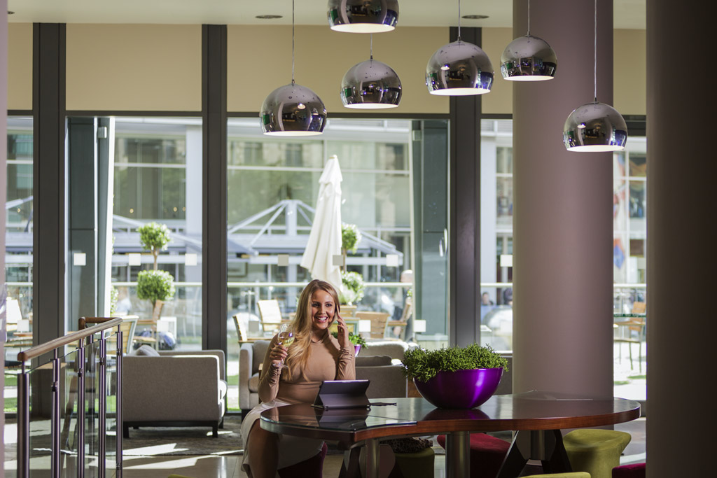 Female working in bar area with tables and chairs and overhead pendant lights.