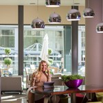 Female working in bar area with tables and chairs and overhead pendant lights.