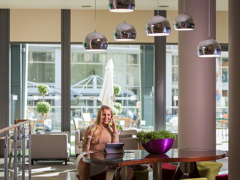 Female working in bar area with tables and chairs and overhead pendant lights.
