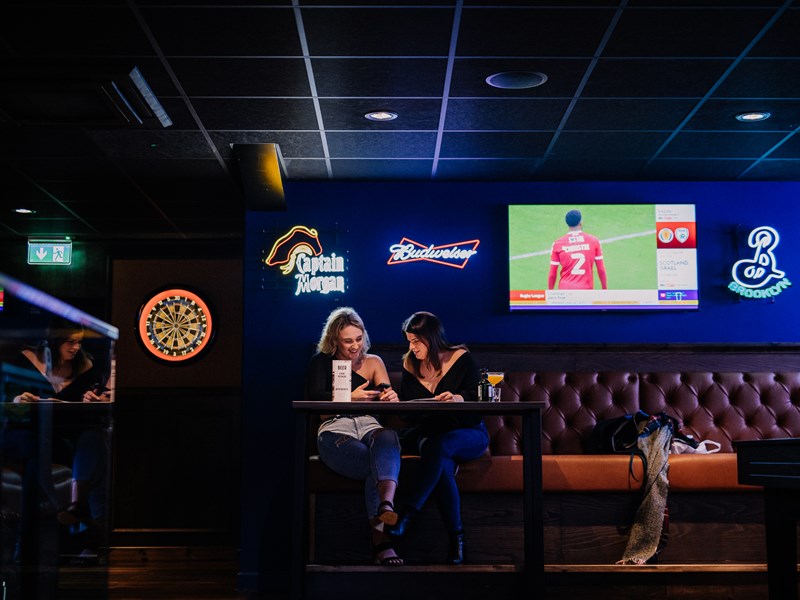 Two people sat at a table having a chat and a drink at The Wildcard Bar & Grill.