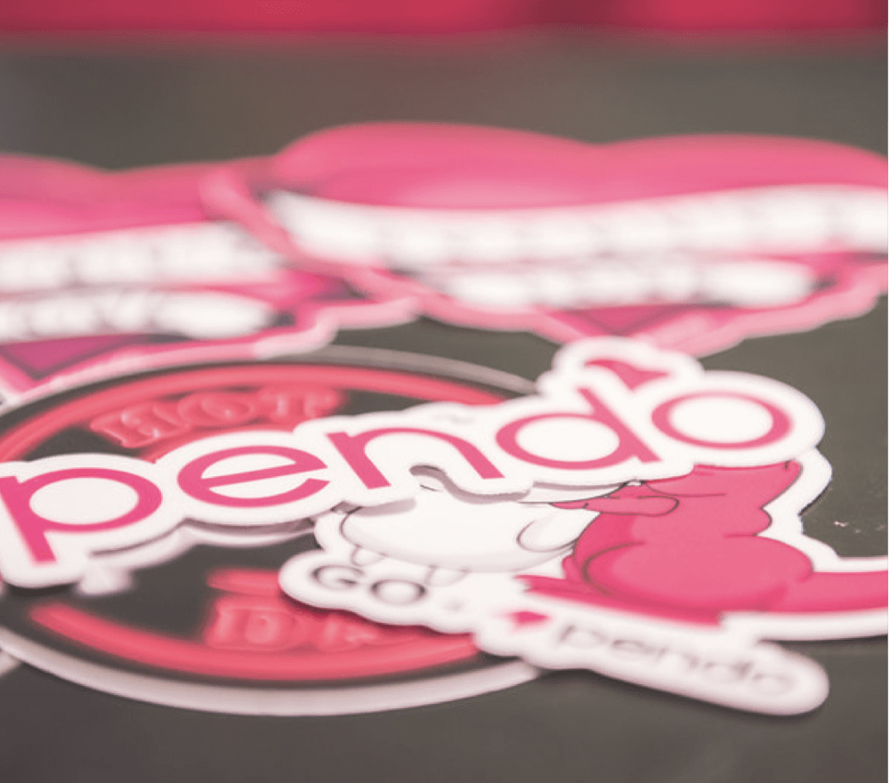 A close up of a dark surface covered in Pendo branded stickers.