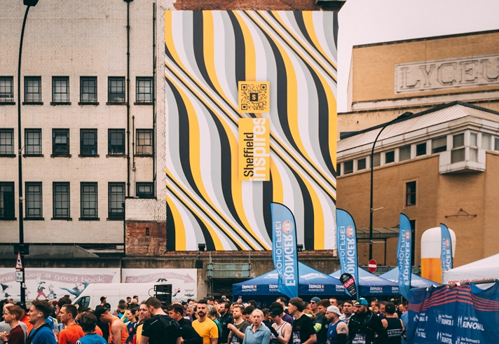 A massive banner on the side of the building shows the distinctive Sheffield Inspires branding as runners gather for Sheffield Half Marathon below it